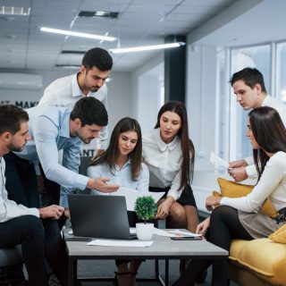 Guy shows document to a girl. Group of young freelancers in the office have conversation and working.